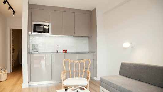 Et moderne rum med gråt køkken, rottingstol og grå sofa. (AI-genereret tekst)