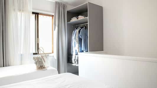 Et værelse med to enkeltsenge, gardiner ved vinduet og et åbent skab med tøj. (AI-genereret tekst)