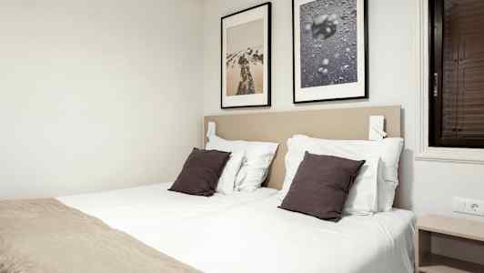 Et soveværelse med to enkeltsenge, hvide lagner, mørke puder og to indrammede billeder på væggen. (AI-genereret tekst)