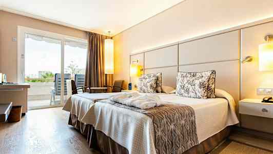 Hotelværelse med to senge og indretning i neutrale toner. Udsigt til balkon gennem glasdøre. (AI-genereret tekst)