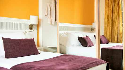 Et hotelværelse med en dobbeltseng, lilla puder og orange vægge. (AI-genereret tekst)