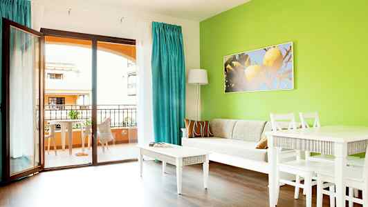 Stue med grøn væg, hvid sofa, hvide møbler og udsigt til altan. (AI-genereret tekst)