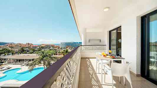 En balkon med udsigt over et poolområde og en resort. (AI-genereret tekst)