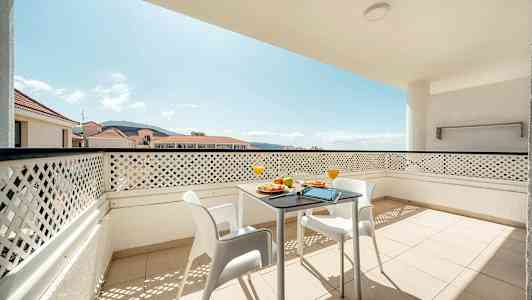 Altan med bord og stole samt udsigt over omkringliggende bygninger og bjerge. (AI-genereret tekst)