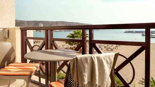 Altan med bord og to stole samt udsigt over stranden og havet. (AI-genereret tekst)