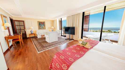 Et rummeligt hotelværelse med dobbeltseng, siddeområde, skrivebord og en balkon med udsigt. (AI-genereret tekst)