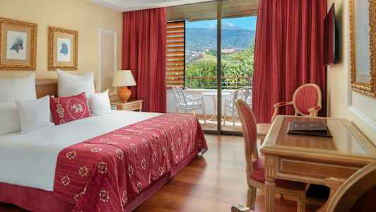 Hotelværelse med dobbeltseng, skrivebord, stol og altan med udsigt til natur og bjerge. (AI-genereret tekst)