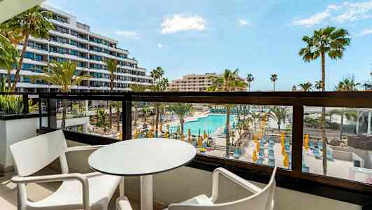 Altan med bord og stole, udsigt over poolområde og omkringliggende bygninger. (AI-genereret tekst)