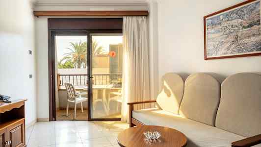 Et hotelværelse med sofa, sidebord og en balkon med udsigt. (AI-genereret tekst)