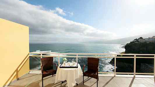 To stole og et bord med dug står på en terrasse med udsigt over havet. (AI-genereret tekst)