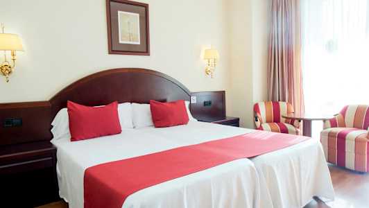 Dobbeltværelse med rødt interiør og to lænestole. (AI-genereret tekst)