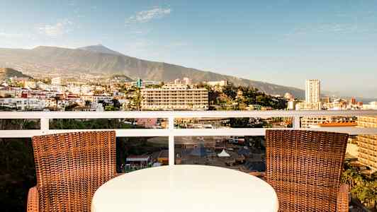 Et bord og to stole på en altan med udsigt over en by og et bjerg i baggrunden. (AI-genereret tekst)