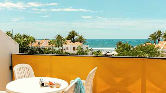 Udsigt fra en altan mod havet med liggestole og grønne omgivelser. (AI-genereret tekst)