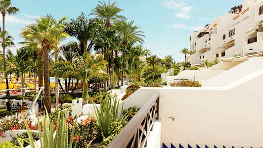 Udsigt over en have med flere svajende palmer og hvide bygninger med terrasser. (AI-genereret tekst)