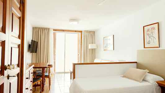 Et værelse med en seng, spisebord, TV og glasdøre, der fører ud til altanen. (AI-genereret tekst)