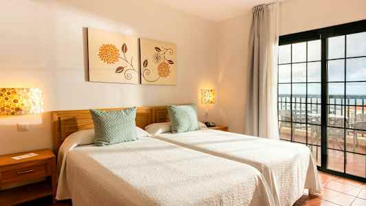 To enkeltsenge med hvidt sengetøj i et rum med udsigt mod en altan. (AI-genereret tekst)