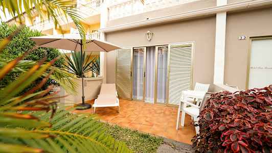 Udendørsterrasse med solseng, parasol og bord med stole, omgivet af vegetation. (AI-genereret tekst)