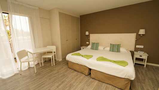 Et hotelværelse med to enkeltsenge, natbord, bord, stole og et skab. (AI-genereret tekst)