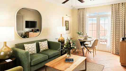 En stue med sofa, sofabord, spiseplads og glasdøre, der fører til en terrasse. (AI-genereret tekst)