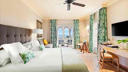 Et hotelværelse med en stor seng, siddeområde, arbejdsbord og havudsigt gennem vinduet. (AI-genereret tekst)