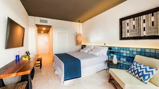 Moderne hotelværelse med dobbeltseng, bord med frugt og en stol. (AI-genereret tekst)