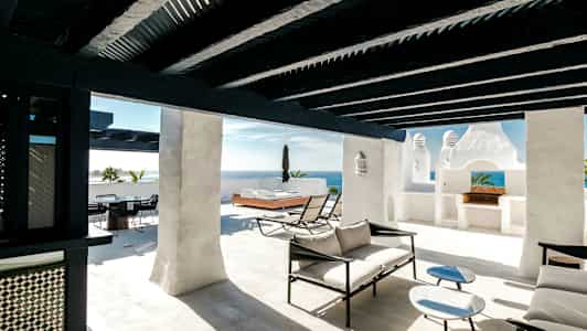 Solrig terrasse med hvide vægge, sorte træbjælker og moderne loungemøbler. (AI-genereret tekst)