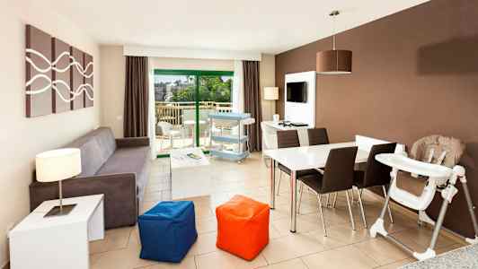 En moderne stue med sofa, spisebord, højstol og udsigt til en balkon. (AI-genereret tekst)