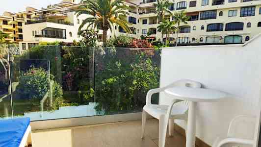 Udsigt fra altan med hvide plastmøbler og omgivet af grøn beplantning. (AI-genereret tekst)