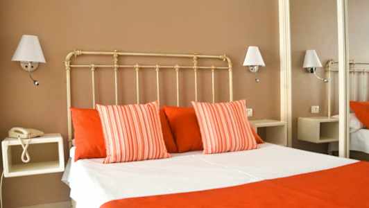 Et hotelværelse med en seng klædt i hvide og røde sengelagner, omgivet af væglamper. (AI-genereret tekst)