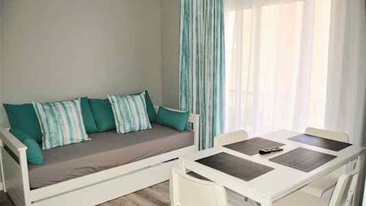 Dagligstue med hvid dagseng og spisebord med fire stole. (AI-genereret tekst)