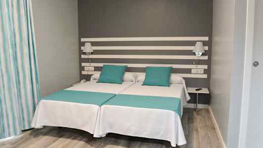 Dobbeltværelse med to enkeltsenge og grå væg. (AI-genereret tekst)