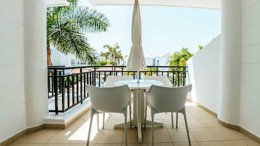 En møbleret balkon med udsigt til palmer og en bygning. (AI-genereret tekst)