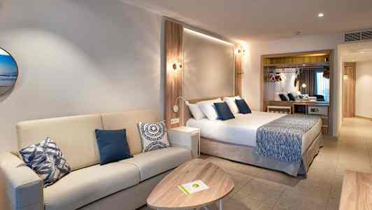 Et hotelværelse med en sofa, et sofabord og en seng med blå dekorative puder. (AI-genereret tekst)