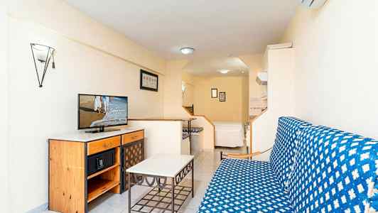 Et studio med en sofagruppe, et bord og en kommode med en TV på. I baggrunden er der en seng. (AI-genereret tekst)