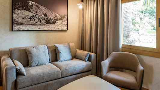 En stue med en grå sofa, en beige lænestol, et hvidt bord og et indrammet billede på væggen. (AI-genereret tekst)