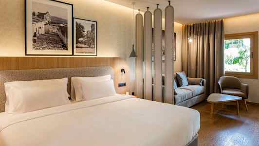 Et hotelværelse med en dobbeltseng, en siddegruppe med sofa og lænestol samt dekorative elementer som billeder på væggen. (AI-genereret tekst)