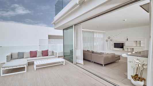 En lys terrasse med sofaarrangement og udsigt til en moderne stue med glasvægge. (AI-genereret tekst)