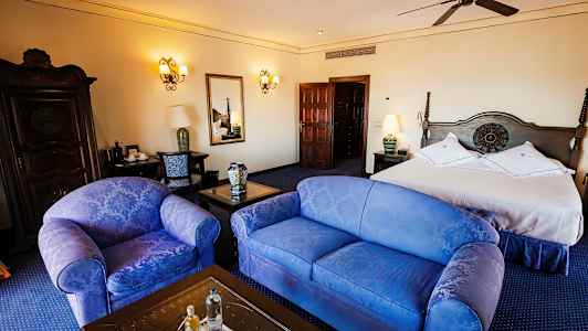 Et hotelværelse med en dobbeltseng, to stole, et bord og en kommode, elegant indrettet. (AI-genereret tekst)