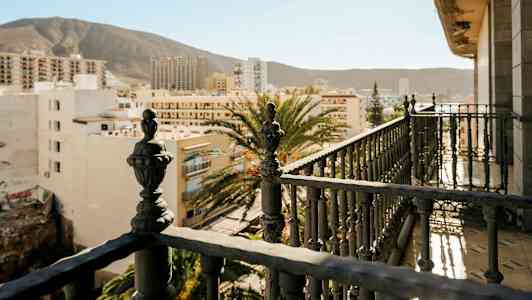 Altan med detaljeret jernrækværk og udsigt over bybygninger med bjerge i baggrunden. (AI-genereret tekst)