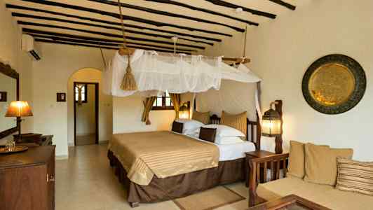 Et hotelværelse med traditionel indretning, en stor seng draperet med et myggenet, en siddegruppe og dekorationer på væggene. (AI-genereret tekst)