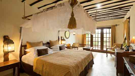 Et soveværelse med en stor seng, myggenet og traditionelle møbler. Vinduer med udsigt. (AI-genereret tekst)