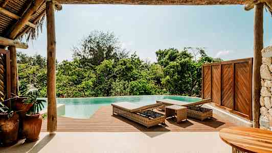 En infinitypool med træterrasse og liggestole i en tropisk omgivelser. (AI-genereret tekst)