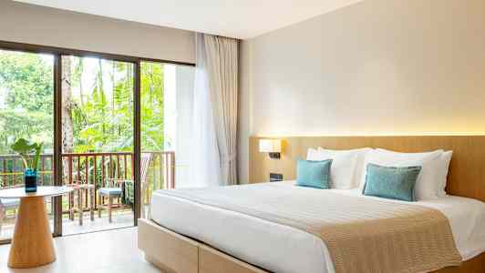 Et hotelværelse med en dobbeltseng, lyse møbler og en altan med udsigt til haven. (AI-genereret tekst)