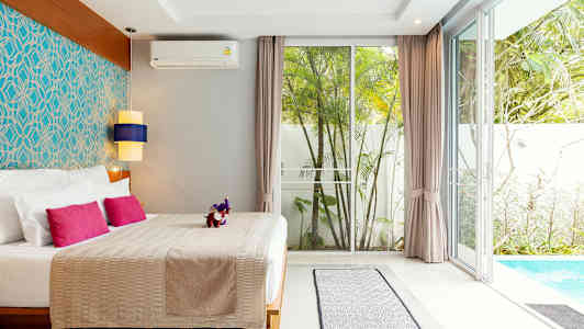 Et soveværelse med dobbeltseng, farverige puder, stilfuld indretning og udsigt til en pool og have. (AI-genereret tekst)