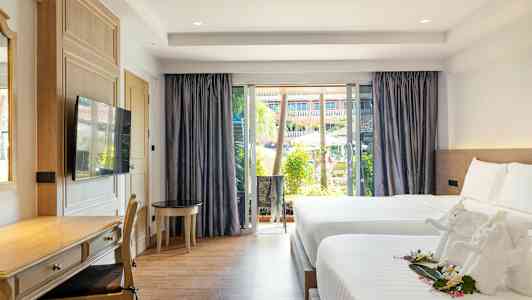 Et hotelværelse med to senge, et skrivebordshjørne og et stort vindue med udsigt over en pool og have. (AI-genereret tekst)