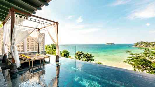 Billedet viser en infinitypool med en solseng under et tag med hvide tekstiler, og i baggrunden ses en sandstrand og havet. (AI-genereret tekst)