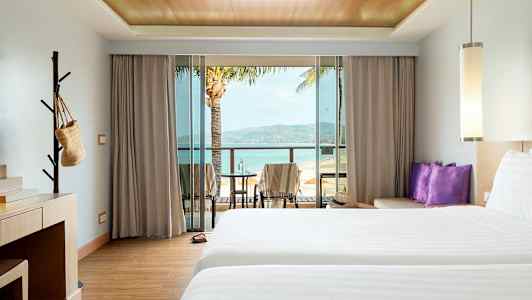 Hotelværelse med to senge, skrivebord og balkon med udsigt over stranden. (AI-genereret tekst)