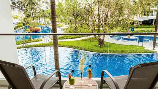 Altan med to stole og et bord med drinks, udsigt over pool og grønt. (AI-genereret tekst)