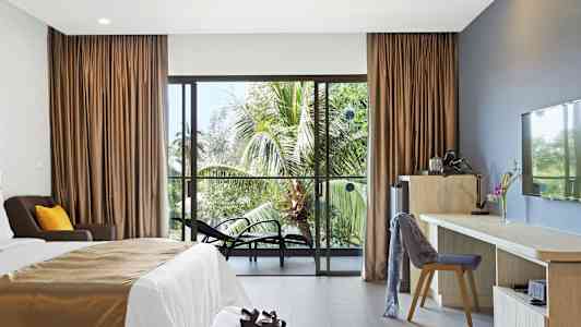 Hotelværelse med en seng, skrivebord og stole, samt udsigt til palmer gennem en glasdør. (AI-genereret tekst)