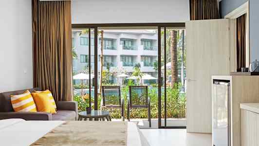 Hotelværelse med seng, sofa og balkon med udsigt til poolområde. (AI-genereret tekst)